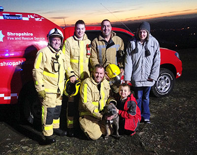 Firefighters and family pose for a group photo in front of a fire service pickup at sunset