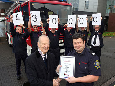 Row of firefighters holding up cards which together spell out £30000