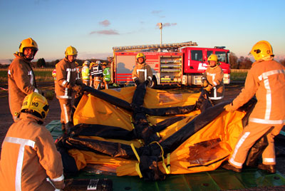 Firefighters erect tent-like structure in front of fire appliance
