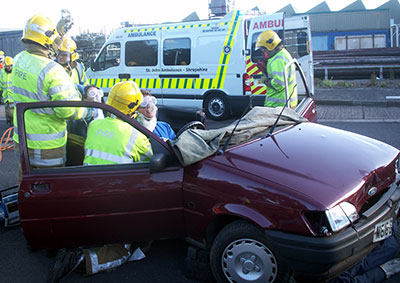Photo of firefighters extracting a lady from the wreckage of a car with an ambulance in the background