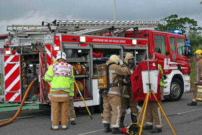 Firefighters prepare breathing apparatus in front of fire appliance