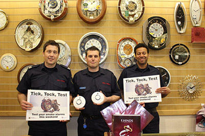  Three firefighters in uniform pictured in front of a wall with a variety of clocks