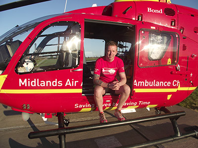 Tim in running gear sitting on the edge of the air ambulance helicopter door on a sunny day