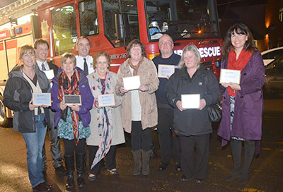 Group shot of employers holding plaques on a dark night in front of a fire appliance