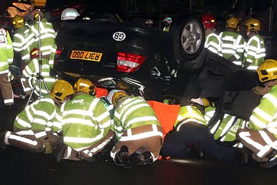 Firefighters attempting to rescue occupants from a car on it's roof