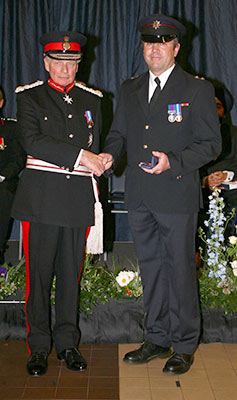 Mac Harris and Sir Algernon Heber-Percy in full undress uniform shake hands and fce towards camera at award ceremony