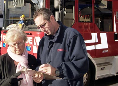 Firefighter speaks with lady, fire appliance in background