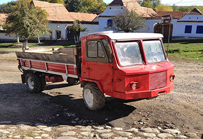 Photo of a very old looking flatbed mini truck in red on a cobbled road