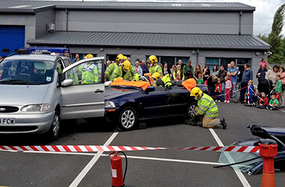 Firefighters work on a roofless car while a crowd look on