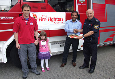 Three men and a young girl pictured in front of a fire appliance with a Firefighters Charity banner