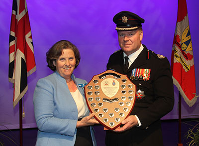 Steve in dress uniform, cap and medals receiving a shield from Diana