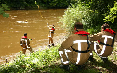 Photo showing a firefighter throwing a float and line out into a river where firefighters are treading water