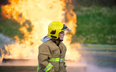 A female firefighter is pictured in protective kit in front of a wall of flames