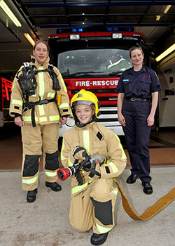 A firefighter in uniform and two taster session women in protective equipment pose to camera