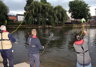 3 people wearing boyancy aids throwing lines to firefighters in the river