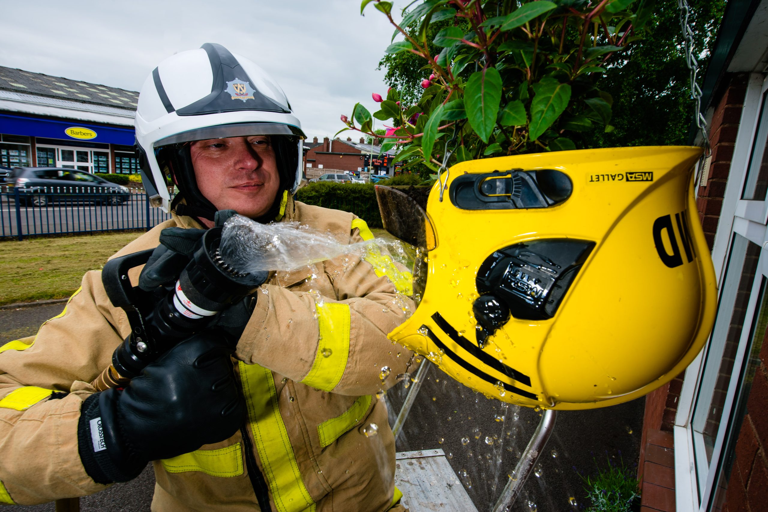 Watch Manager Mark Smith with the recycled helmet used as a flower basket outside Market Drayton fire station in Shropshire. Image courtesy Shropshire Star